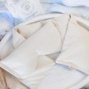 May include: Two white cotton eye pillows with the text "Frankie Jo" printed on each. The pillows are on a white round tray.