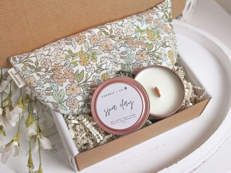 Puede incluir: Un set de regalo para un d&iacute;a de spa en una caja de cart&oacute;n. El set incluye una almohada para los ojos con estampado floral, una vela en una lata de oro rosa con las palabras "Spa Day" y papel triturado. La vela tiene una mecha de madera.