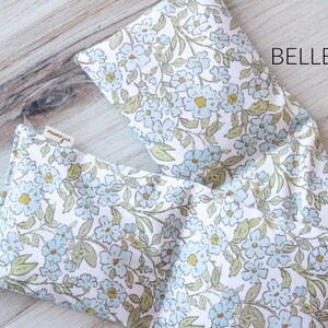 May include: Two rectangular fabric items with a floral pattern. The pattern features light blue flowers, green leaves, and yellow centers on a white background. The word "BELLE" is printed in black. A small tag reads "frankie & co."