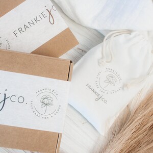 K&ouml;nnte beinhalten: Zwei braune Pappkartons mit wei&szlig;en Etiketten. Die Etiketten zeigen ein Blumenmuster und den Text "Frankie jco. Self care for a cause". Im Hintergrund befindet sich ein wei&szlig;er Kordelbeutel mit einem &auml;hnlichen Blumenmuster und dem Text "Frankie jco. Self care for a cause".