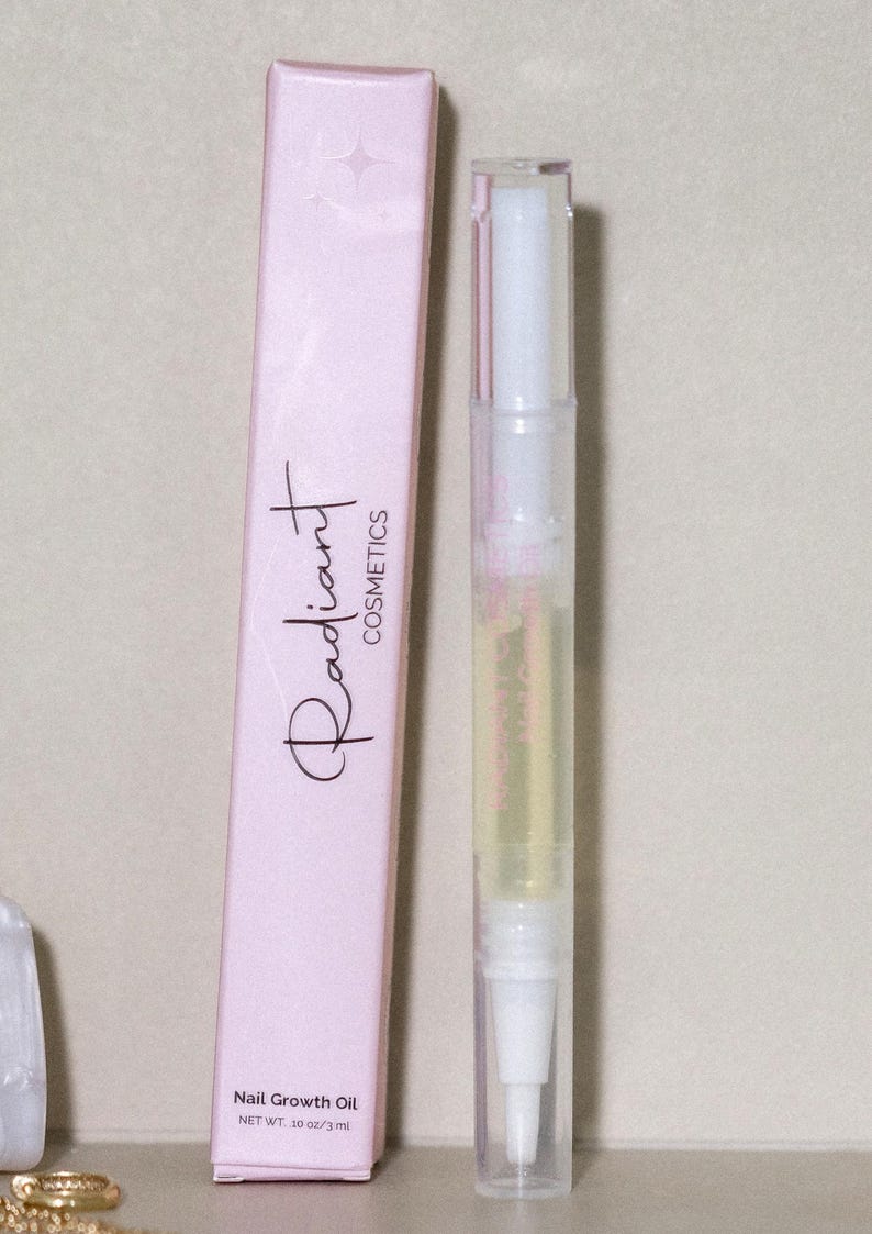 May include: A light pink box and a clear nail oil pen are displayed. The box has the words "Radiant Cosmetics" in a script font. The pen is filled with a yellow liquid and has a brush tip. The box reads "Nail Growth Oil NET WT. 10 oz/3 ml."