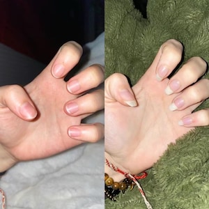 May include: Two hands with natural nails are shown side by side. One hand has short, trimmed nails, while the other has longer, more squared-off nails. The skin tone is fair, and the background is a soft, neutral color.