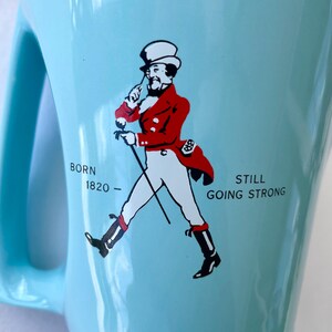 Pode incluir: Caneca de cer&acirc;mica azul clara com uma al&ccedil;a grande. A caneca apresenta um gr&aacute;fico de um homem com um casaco vermelho e cal&ccedil;as brancas, andando com uma bengala. O texto na caneca diz "BORN 1820 - STILL GOING STRONG."