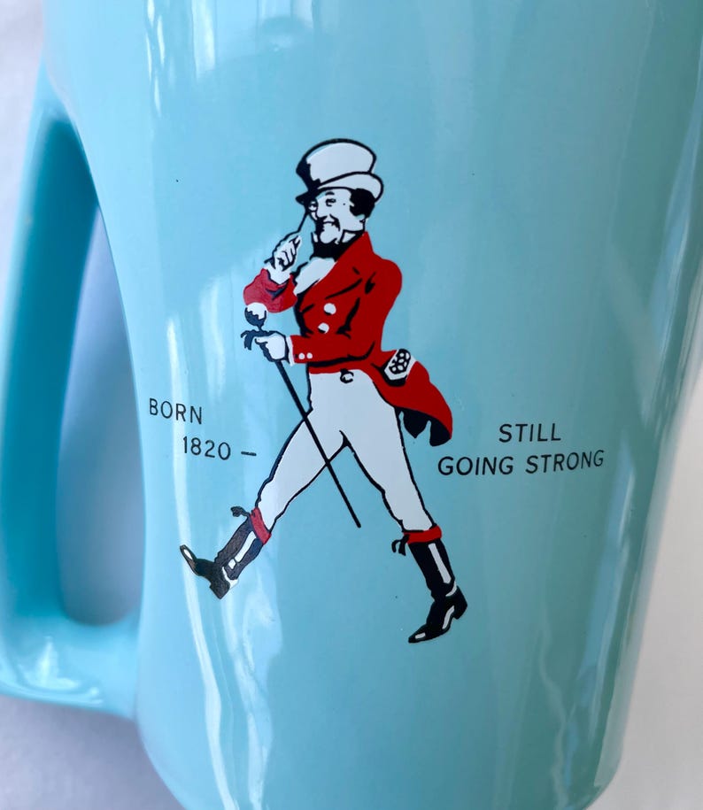 Pode incluir: Caneca de cer&acirc;mica azul clara com uma al&ccedil;a grande. A caneca apresenta um gr&aacute;fico de um homem com um casaco vermelho e cal&ccedil;as brancas, andando com uma bengala. O texto na caneca diz "BORN 1820 - STILL GOING STRONG."