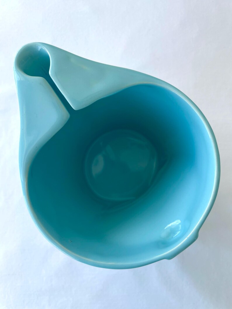 Pode incluir: Uma tigela de cer&acirc;mica turquesa com um design assim&eacute;trico &uacute;nico. A tigela apresenta uma extens&atilde;o curva em forma de al&ccedil;a e um interior profundo. O acabamento brilhante real&ccedil;a a cor vibrante, tornando-a uma pe&ccedil;a decorativa marcante.