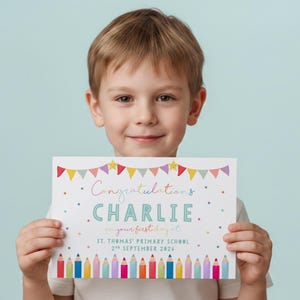 May include: A rectangular white sign featuring colourful bunting at the top, the text Congratulations CHARLIE on your first day at ST. THOMAS' PRIMARY SCHOOL 2nd SEPTEMBER 2026, and a row of multicoloured pencils along the bottom edge.