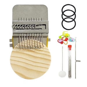May include: A metal darning loom tool with a round wooden base, three black elastic hair ties, a set of colorful plastic stitch markers, a needle case containing multiple sewing needles, and a long metal hook tool for textile repair.