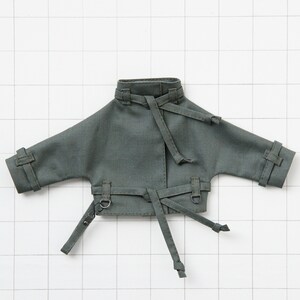 May include: A dark green jacket with a tie belt and long sleeves. The jacket has a collar and two pockets on the front.