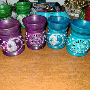 May include: Set of six tealight holders made of carved soapstone. Each holder features a different design of a sun and moon with intricate details. The holders are in shades of purple, teal, and green.
