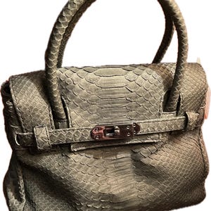 Puede incluir: Un bolso verde salvia con un patrón de piel de serpiente texturizado. El bolso tiene un asa superior, un cierre de solapa con un cierre plateado y una correa a juego. El diseño es estructurado y elegante, adecuado para diversas ocasiones.
