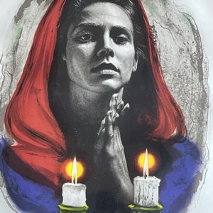 May include: A woman in a red hooded cloak with her hands clasped in prayer. Two lit candles are in front of her, one on each side. The background is a watercolor wash of blue, green, and gray.