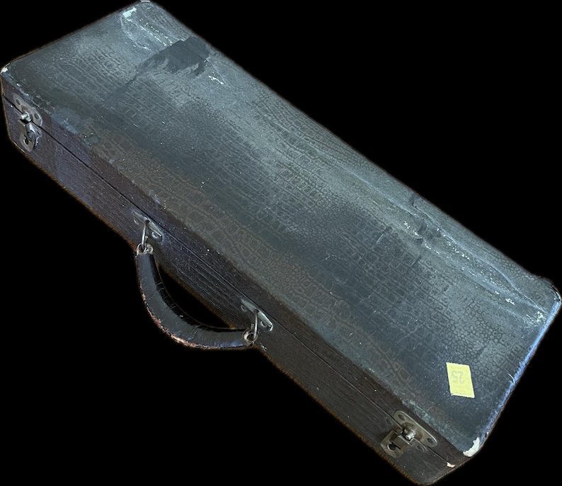 K&ouml;nnte beinhalten: Ein rechteckiger, schwarzer Vintage-Koffer mit strukturierter Oberfl&auml;che und gebogenem Griff. Der Koffer hat Metallverschl&uuml;sse und Scharniere, und ein kleiner gelber Aufkleber ist an der Seite angebracht. Der Koffer scheint aus einem strapazierf&auml;higen Material zu bestehen.