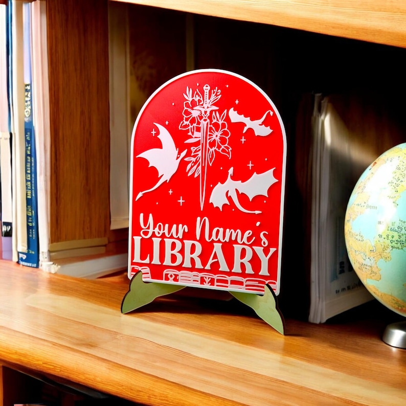 May include: Red wooden sign with a white dragon design and the text "Your Name's Library". The sign is on a wooden stand.