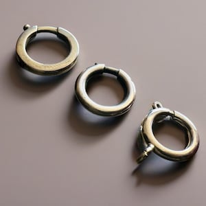 以下が含まれることがあります： 斜めに配置された3つの円形の銀色のスプリングリングクラスプ。各クラスプには開閉用の小さなレバー機構があり、磨かれた金属仕上げと滑らかで丸みを帯びたプロファイルが特徴で、ジュエリー製作や修理に適しています。