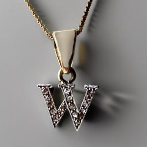 以下が含まれることがあります： Wの形をしたペンダントがついた金のチェーンネックレス。文字には小さなダイヤモンドが埋め込まれています。