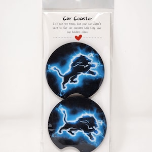 May include: Two black car coasters with a blue and white image of a lion with lightning bolts. The text "Car Coaster" is printed on the packaging. "Life can get messy, but your car doesn't have to. Our car coasters help keep your cup holders clean." is printed on the packaging.