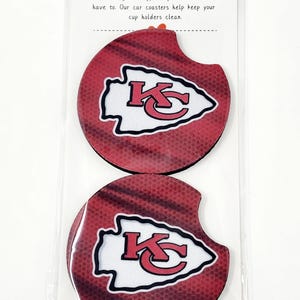 May include: Two round car coasters with a red, white, and black Kansas City Chiefs logo. The coasters are made of a soft, absorbent material and are designed to protect your car's cup holders from spills and stains. "Car Coaster" and "Life can get messy, but your car doesn't have to. Our car coasters help keep your cup holders clean." are printed on the packaging.