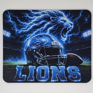 May include: A rectangular mouse pad featuring a blue and black graphic of a roaring lion surrounded by lightning. A football helmet with a lion logo and a football are centered in a stadium setting. The word LIONS is printed in large blue letters.