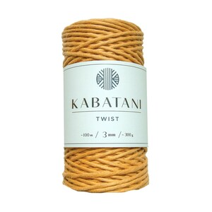 Może przedstawiać: Szpula 3 mm grubego, musztardowo-ż&oacute;łtego sznurka bawełnianego z etykietą "Kabatani Twist - 100m / 3mm / 300g".