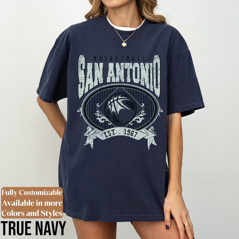 Może przedstawiać: Granatowa koszulka z nadrukiem koszyk&oacute;wki i napisem "BASKETBALL SAN ANTONIO EST 1967". Koszulka ma wygląd vintage. Widoczny jest r&oacute;wnież tekst "Fully Customizable Available in more Colors and Styles TRUE NAVY".