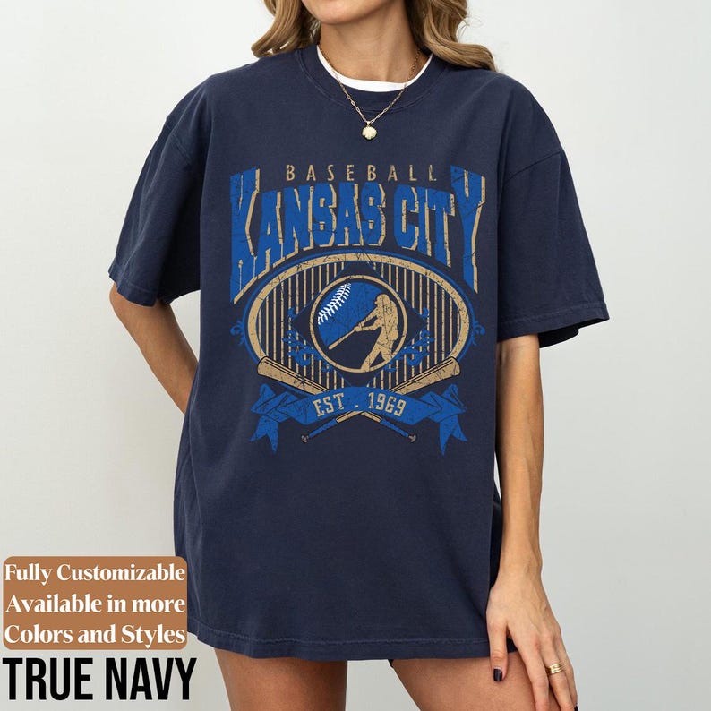 May include: Navy blue baseball t-shirt with a distressed graphic design. The design features the text "BASEBALL KANSAS CITY" above an oval emblem with a baseball player silhouette, baseball, and crossed bats. The text "EST. 1969" is also included.