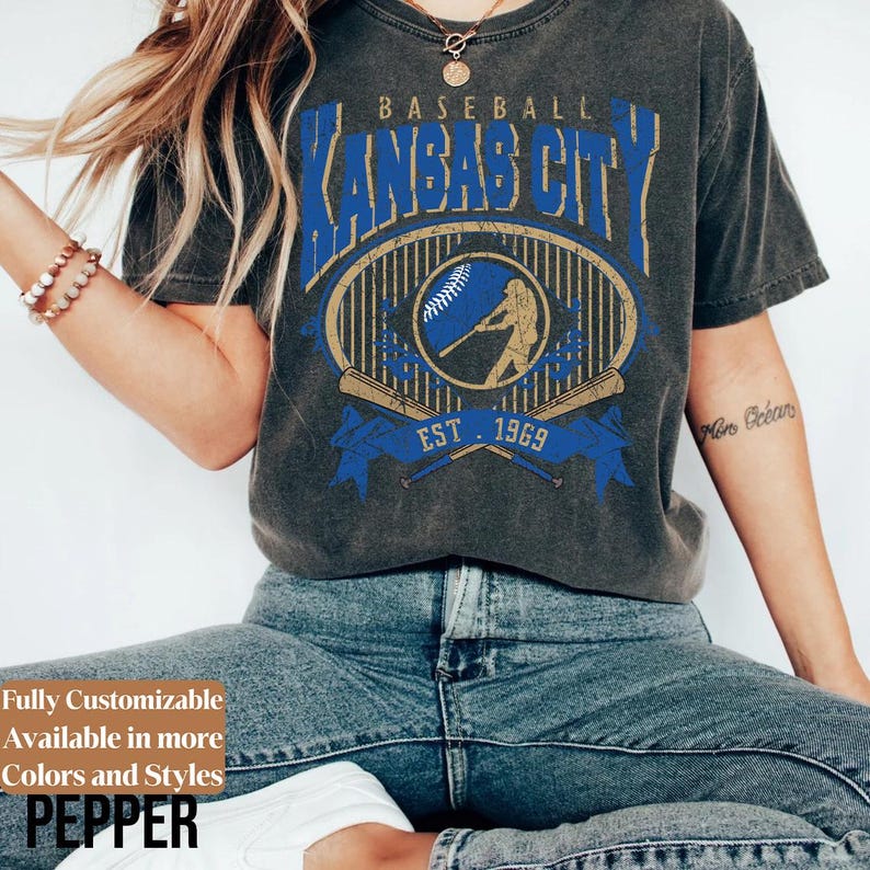 May include: Dark gray t-shirt featuring a distressed graphic design with the text "Kansas City Baseball" in blue and gold. The design includes a baseball, a batter silhouette, and the year "1969".
