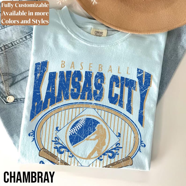 May include: Light blue t-shirt with a distressed graphic that says "Baseball Kansas City". The design includes a baseball, a batter silhouette, and baseball bats. The word "Chambray" is at the bottom.