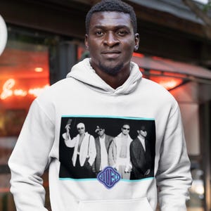 May include: A white hoodie with a black and white image of five people wearing sunglasses and hats. The image is framed in a light blue border and the word "COOCH" is printed in a purple circle below the image.