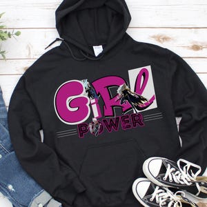 May include: Black hooded sweatshirt with the words "GIRL POWER" in a pink and white design. The sweatshirt features a front pocket and a drawstring hood. A pair of black and white sneakers are at the bottom right.