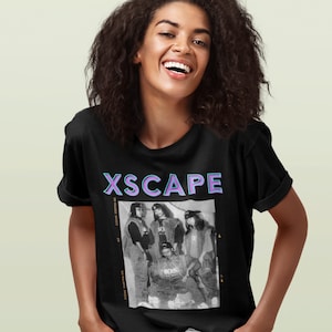May include: Black t-shirt with a graphic print of the girl group Xscape. The print features a black and white photo of the group with the text "XSCAPE" in purple and blue letters.