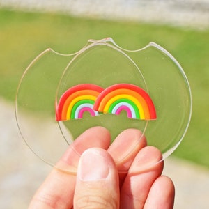May include: Two rainbow-colored silicone coasters with a clear acrylic base. The coasters are held in a hand.