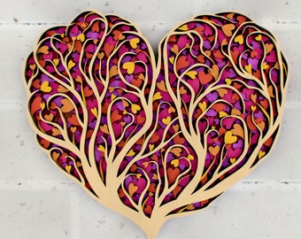 Pode incluir: Uma decoração de parede de madeira em forma de coração com um design em camadas de corações cortados de forma intrincada em tons de rosa, roxo e laranja.