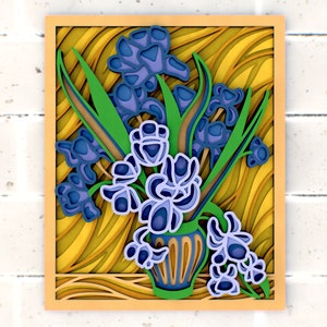 Peut inclure: Une œuvre d'art en papier encadrée représentant un bouquet de fleurs bleues et violettes dans un vase vert. L'arrière-plan est un motif rayé jaune et brun.