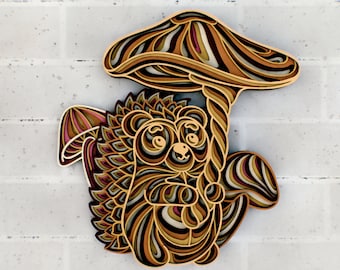 May include: A layered papercraft design of a brown and tan hedgehog with a mushroom on its back. The mushroom has a brown and tan striped cap and a brown stem.