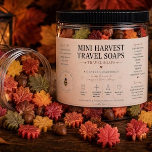 May include: A clear plastic jar filled with small, leaf and acorn-shaped soaps in autumn colors of red, orange, yellow, and green. The label reads Mini Harvest Travel Soaps, Gentle Cleansing, and lists ingredients like goat's milk and shea butter.