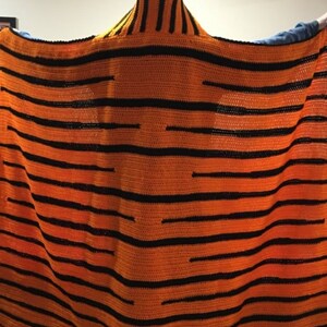 Peut inclure: Une couverture en crochet en forme de tigre avec des rayures orange et noires. La couverture a une capuche avec des oreilles de tigre.