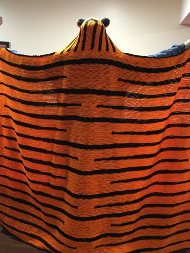 Peut inclure: Une couverture en crochet en forme de tigre avec des rayures orange et noires. La couverture a une capuche avec des oreilles de tigre.