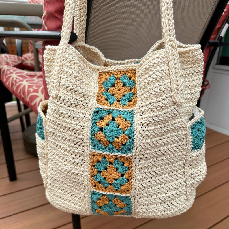 An off white crochet bag with a blue and brown granny square stripe running down the middle.
