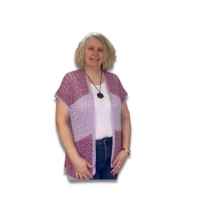 May include: A woman wearing a light purple and lavender crochet cardigan with short sleeves. She is wearing a white t-shirt underneath and blue jeans.