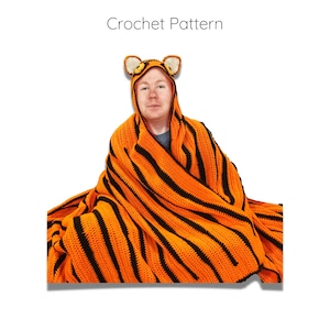 Peut inclure: Une personne portant une couverture en crochet &agrave; rayures de tigre avec une capuche assortie en forme de t&ecirc;te de tigre. La couverture est orange et noire avec un motif ray&eacute;.