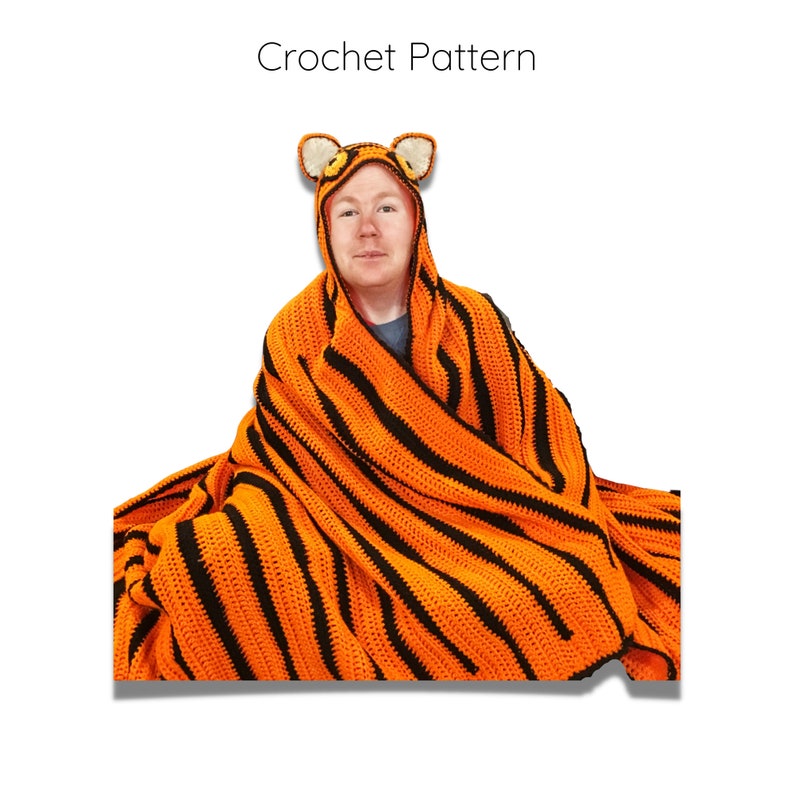 Peut inclure: Une personne portant une couverture en crochet &agrave; rayures de tigre avec une capuche assortie en forme de t&ecirc;te de tigre. La couverture est orange et noire avec un motif ray&eacute;.