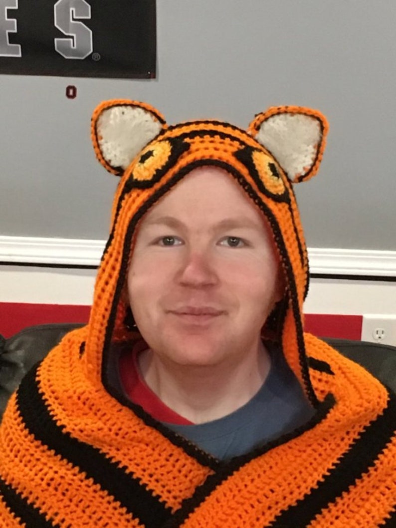 Peut inclure: Une personne portant une couverture &agrave; capuche en crochet &agrave; rayures orange et noires avec des oreilles de tigre.