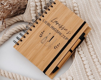 May include: A wooden recipe journal with a black spiral binding and a pen. The journal has the text "Larissa's Lieblingsrezept" engraved on the front.