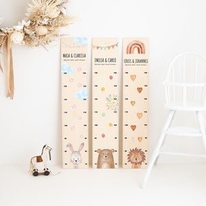 Könnte beinhalten: Drei Holz-Wachstumstabellen mit verschiedenen Tierillustrationen und Namen. Die Tabellen sind mit Wolken, Sternen, Feuerwerk und Herzen verziert. Die Namen auf den Tabellen sind "Maja & Clarissa", "Emilia & Carlo" und "Louis & Johannes".