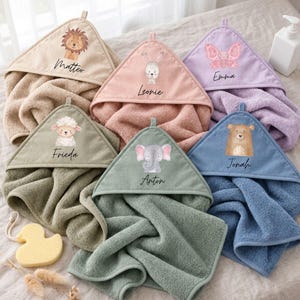 Peut inclure: Six serviettes à capuche en beige, rose, lavande, vert sauge, vert olive et bleu. Chaque serviette présente une illustration aquarelle d'animal : lion, lapin, papillon, mouton, éléphant ou ours, avec les prénoms Matteo, Leonie, Emma, Frieda, Anton et Jonah.