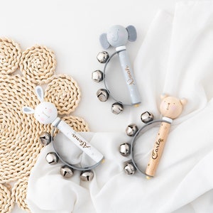 Può includere: Tre sonagli di legno per bambini con manici a forma di testa di animale e campanelli d'argento. I sonagli sono personalizzati con i nomi "Alena", "Noora" e "Carlo".
