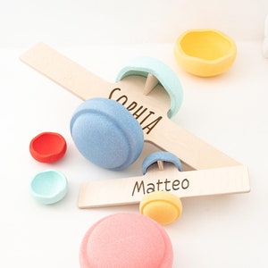 Op de afbeelding: Houten speelgoedvliegtuig met kleurrijke viltstukken, waaronder een blauwe, roze, gele en groene. Het vliegtuig heeft de namen "Sophia" en "Matteo" erop geschreven.