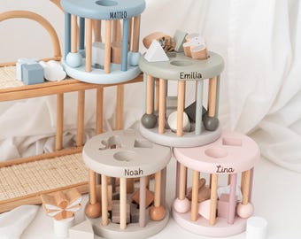 May include: Four wooden toy activity centers with different colored bases and personalized names: Matteo, Emilia, Noah, and Lina. Each center features a variety of shapes and colors for children to explore.