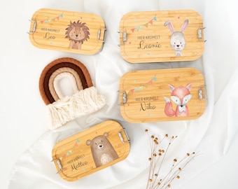 May include: Four rectangular bamboo lunch boxes with metal latches, each featuring a colourful bunting illustration and the text "HIER KRÜMELT" followed by the names Leo, Leonie, Niko, or Matteo, alongside a lion, rabbit, fox, or bear graphic.