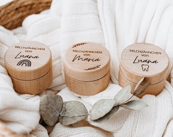 May include: Three small wooden boxes with lids, each engraved with the words "Milchzähnchen von" followed by a name: "Luana", "Maria", and "Luana". Each box has a unique design: a rainbow, leaves, and a tooth.